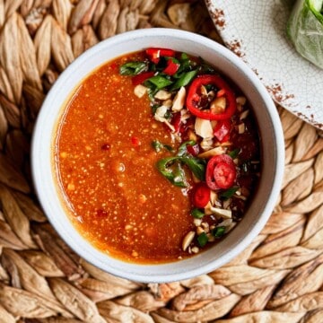 Bowl of peanut sauce garnished with sliced red chili and peanuts, served with fresh spring rolls.