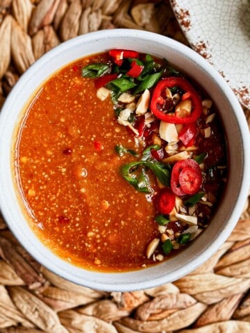 Bowl of peanut sauce garnished with sliced red chili and peanuts, served with fresh spring rolls.