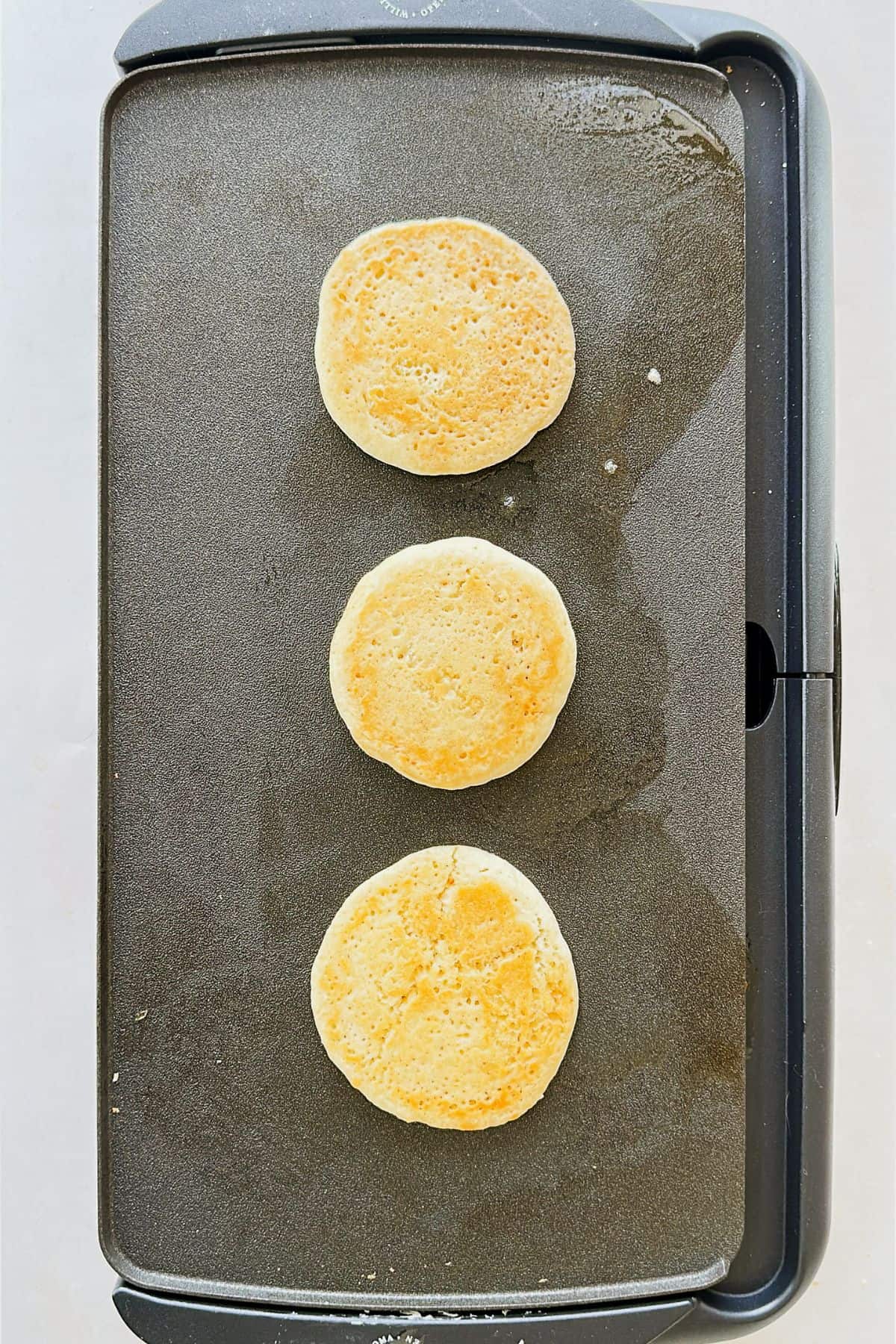 Vegan pancakes flipped on a griddle, showing lightly golden brown bottoms.