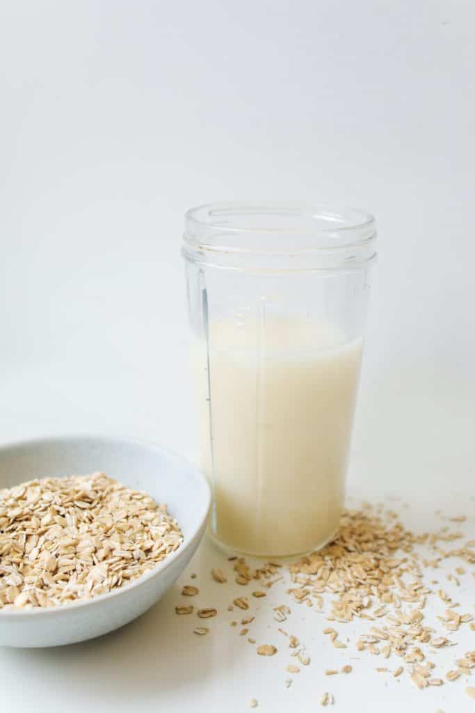 oat milk in clear glass jar plus oatmeal in a bowl and spread on table