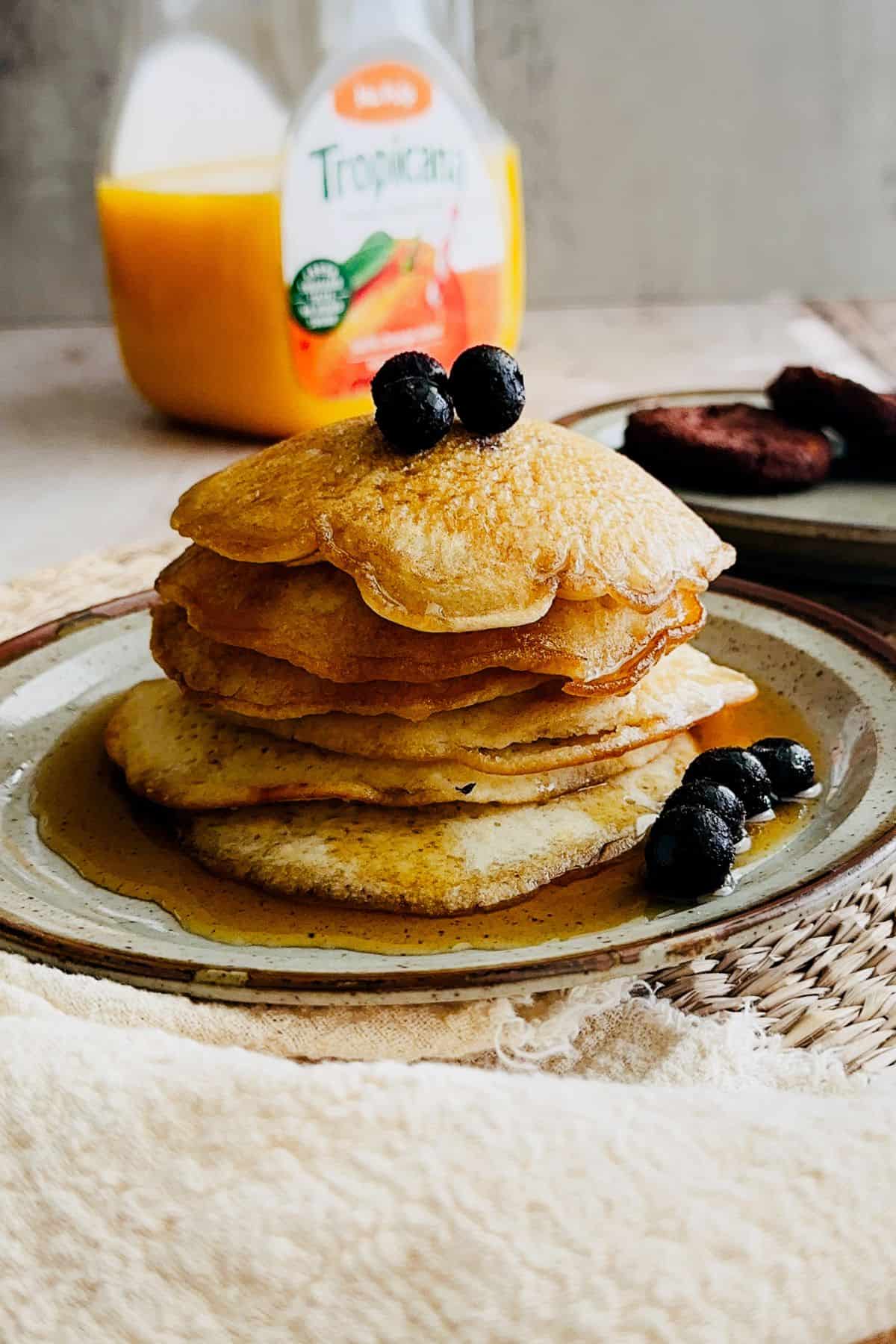 Stack of fluffy vegan pancakes topped with blueberries and maple syrup on a ceramic plate.