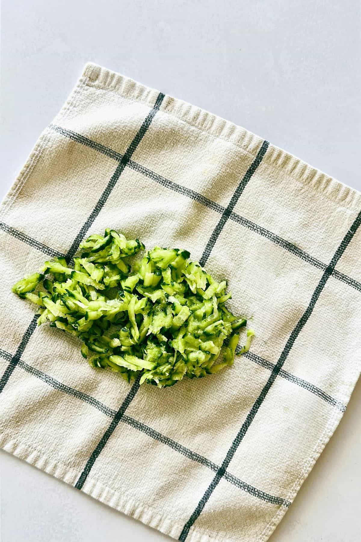 Tzatziki ingredients in a bowl grated cucumber on a towel.