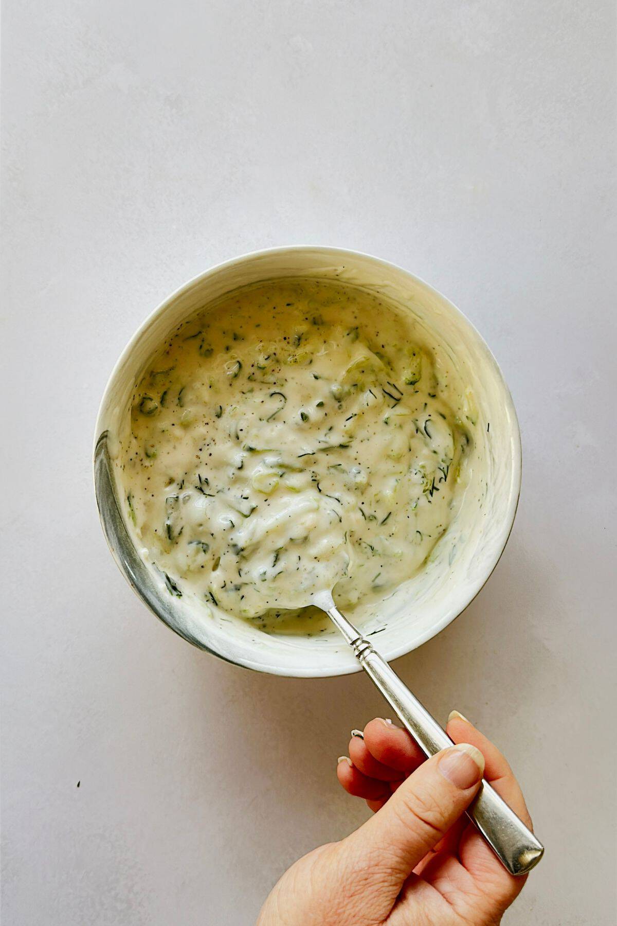 Tzatziki ingredients in a bowl someone stirring the vegan tzatziki with a spoon.