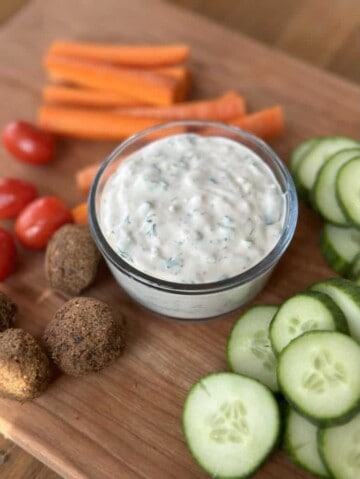 Tzatziki sauce surrounded by veggies and falafel on wooden board