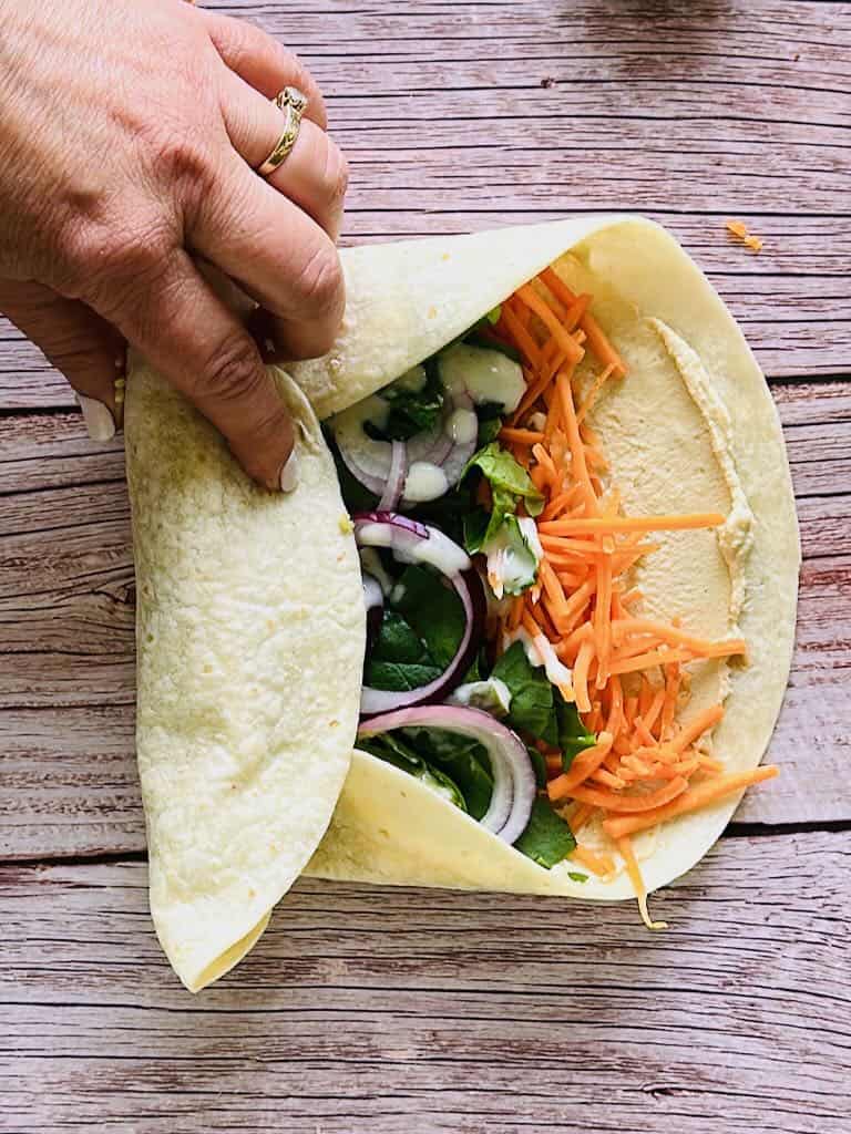 Folding the vegan falafel wrap to show how to wrap a tortilla