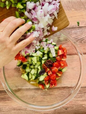 Tossing vegetables in a bowl for the Vegan Greek Salad