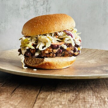 chipotle black bean burger topped with vegan coleslaw on a plate, side view.