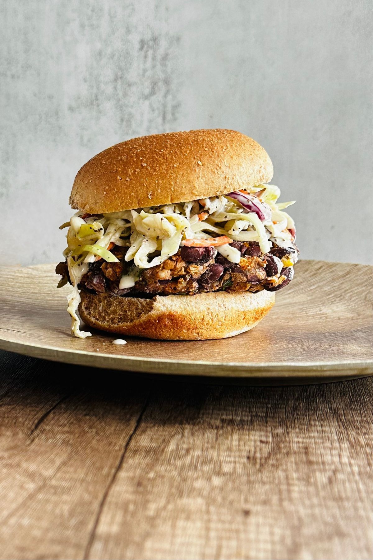 hand holding a chipotle black bean burger on a bun with chipotle red pepper sauce, lettuce, red onions, tomato, and avocado