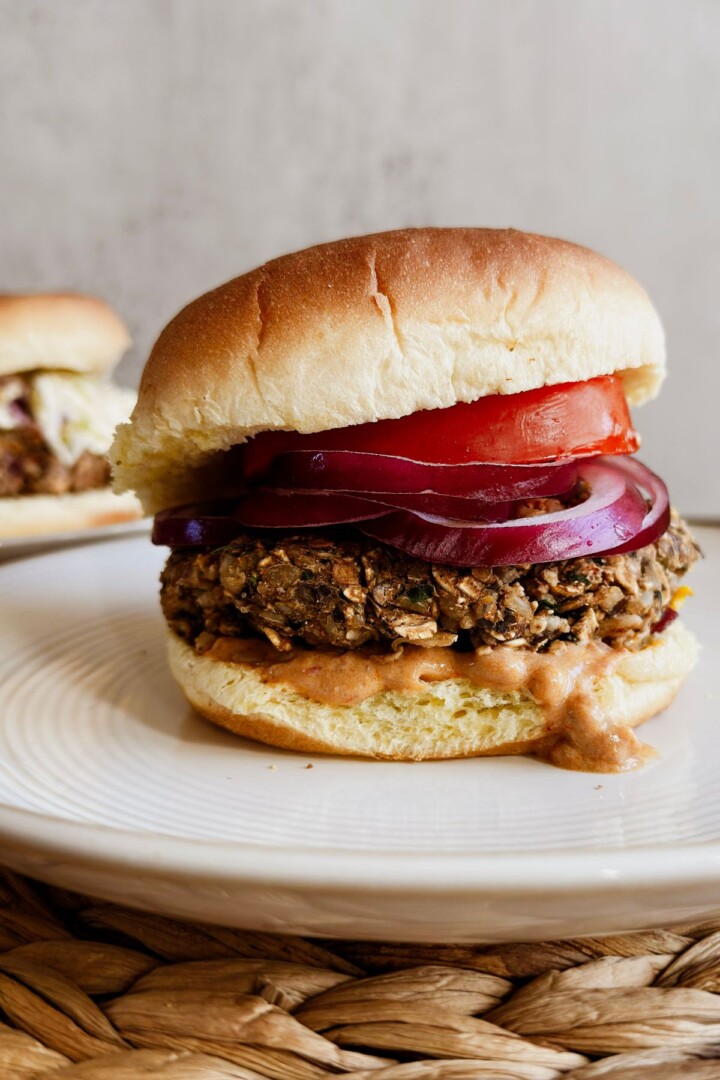 chipotle black bean burger topped with red onions, tomatoes, and vegan chipotle mayo, side view.