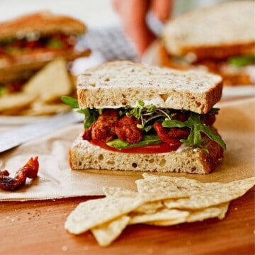Vegan BLT sandwich with soy curls on parchment paper; side view.