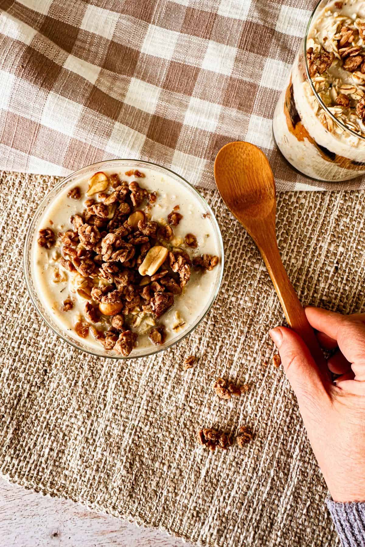 top view of Vegan PB-J overnight oats in a glass with a hand grabbing a spoon