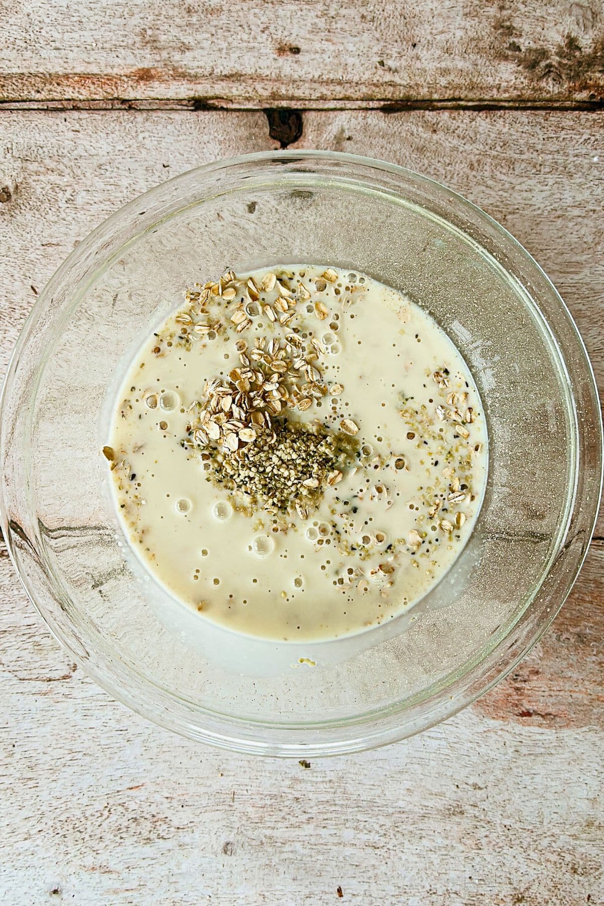 top view of clear glass bowl with oats, vegan milk, and hemp seeds