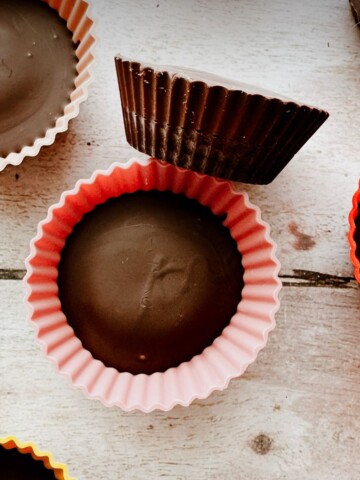 peanut butter cups in silicone holders on a table. One is removed from the silicone muffin wrap and laying on its side.