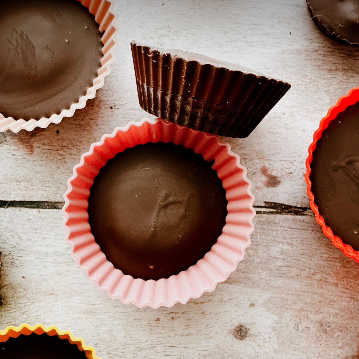 peanut butter cups in silicone holders on a table. One is removed from the silicone muffin wrap and laying on its side.