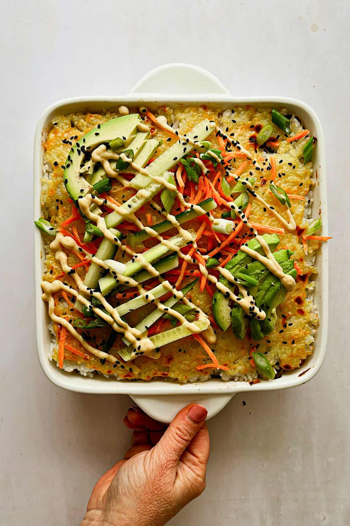 hand bringing out the sushi bake with the garnishes and placing on the table 