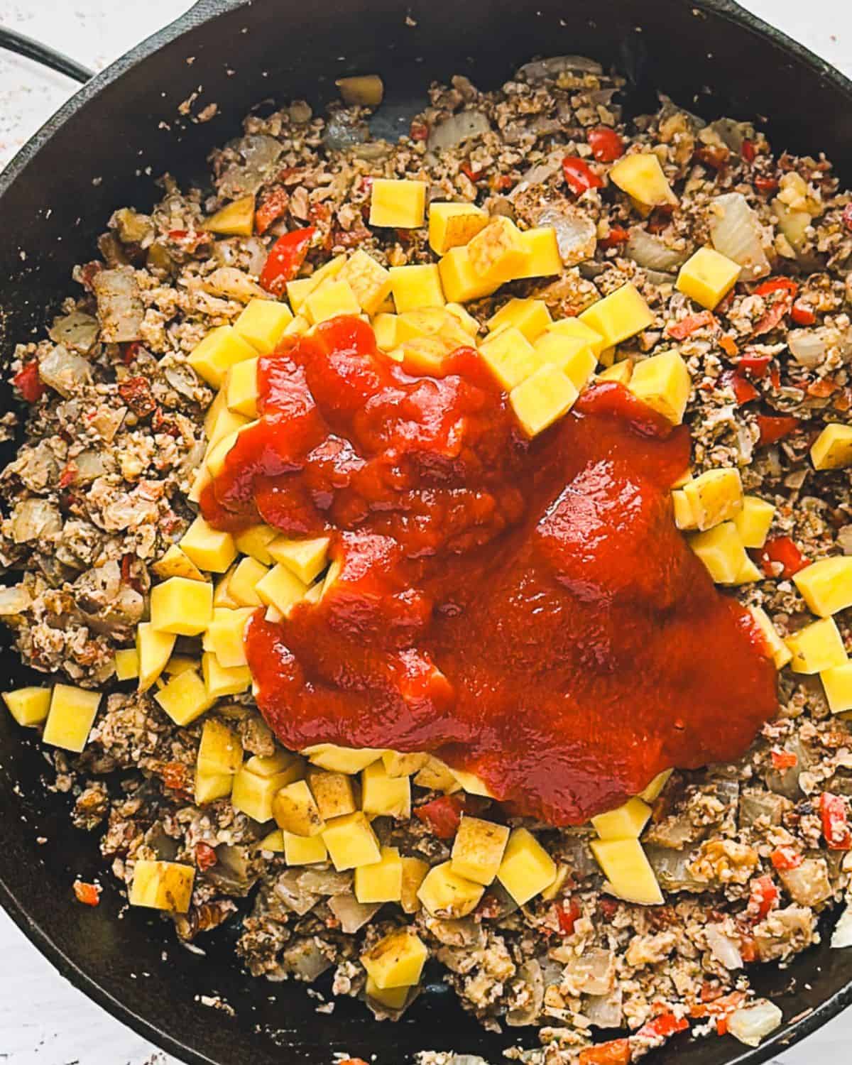 Step 6: adding potatoes and tomato sauce to vegan picadillo. Adding remaining ingredients such as broth, olives, capers, bay leaf and raisins.