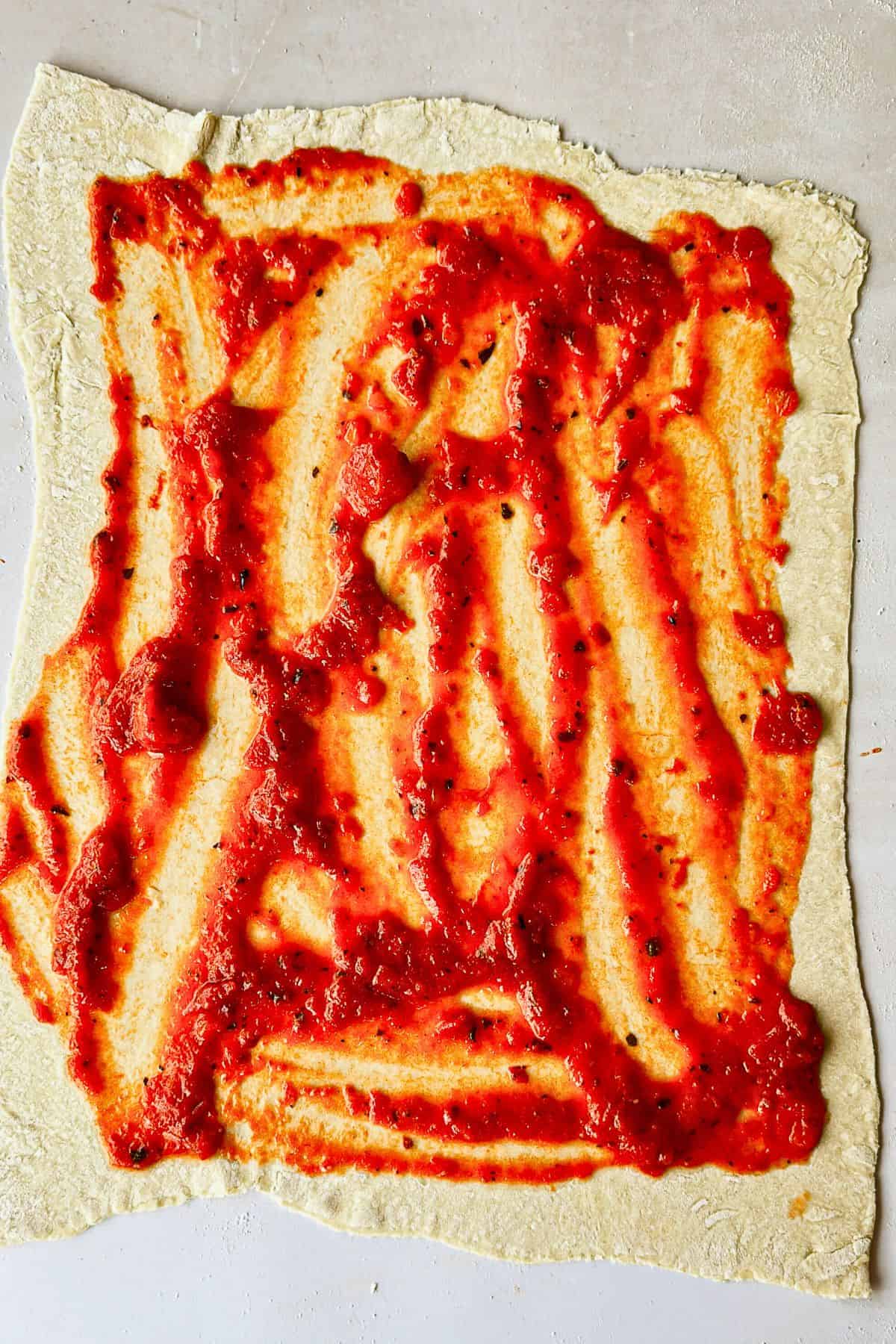 adding sauce to dough for vegan pizza rolls