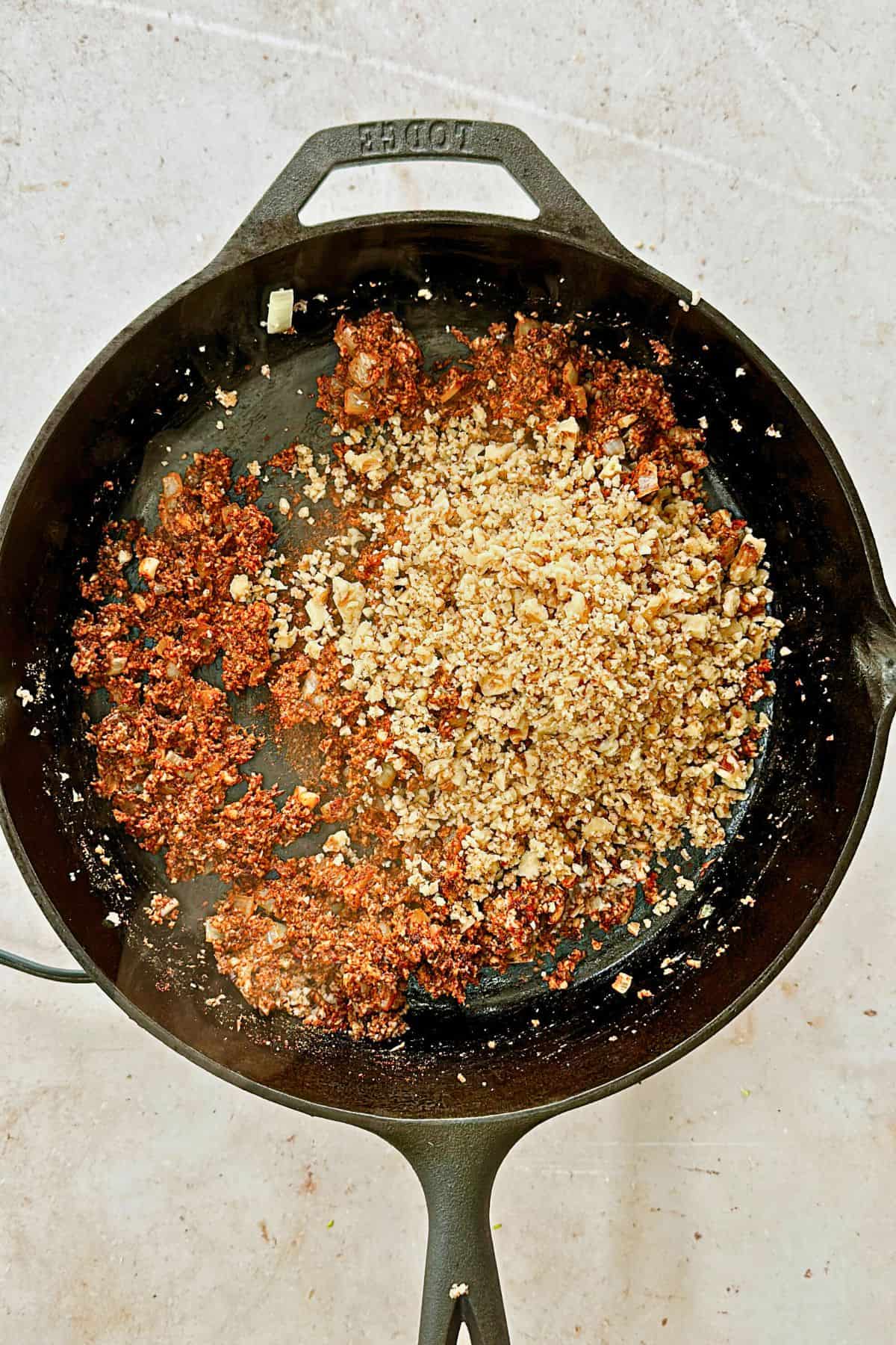 adding walnuts to mushrooms and onions in a cast iron pan; top view