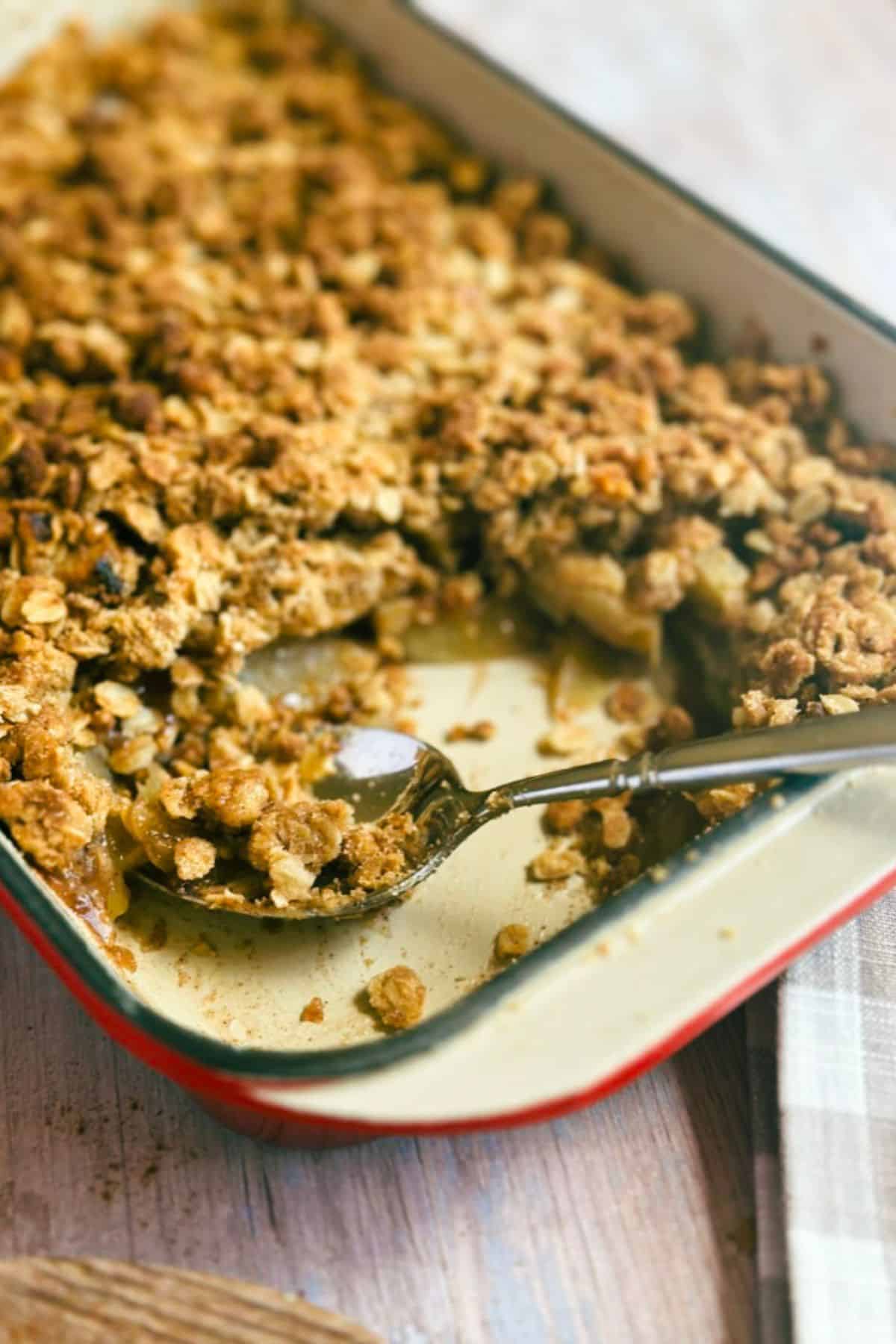 vegan apple crisp in a baking dish with a serving spoon