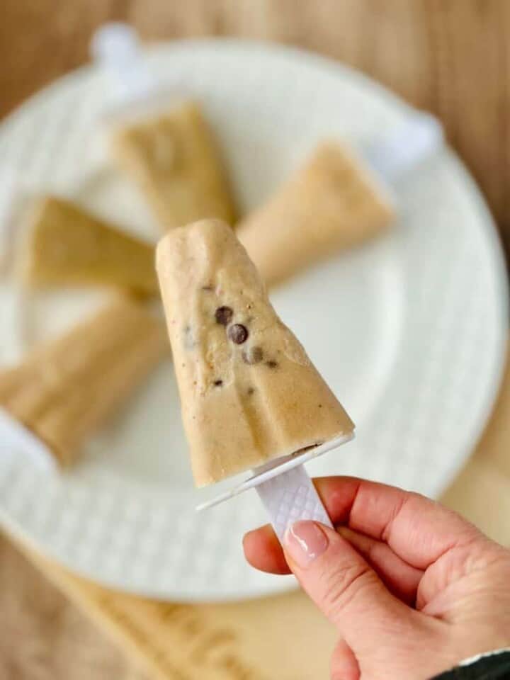 banana popsicle with chocolate chips held by a hand over a dish of other popsicles in the background