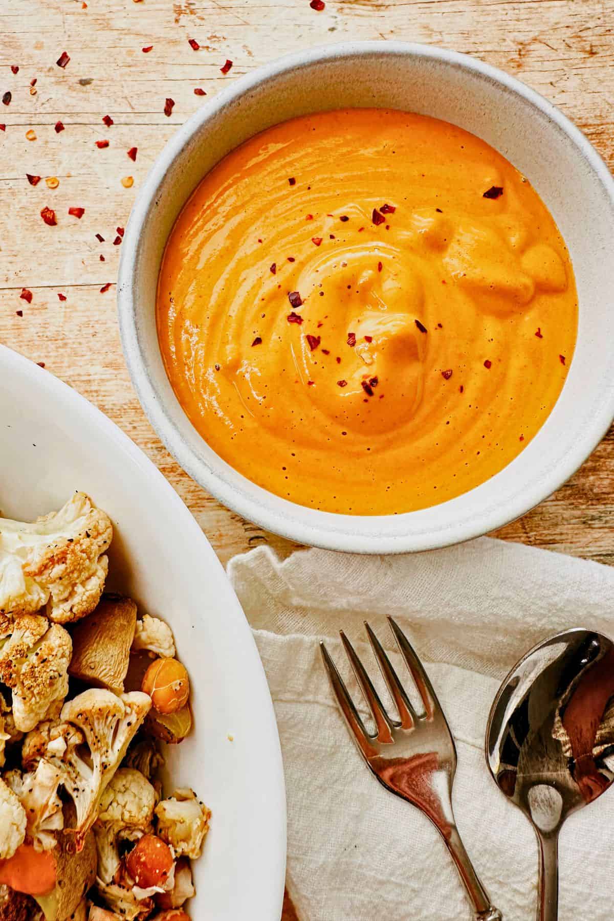 Vegan Cashew Cheese Sauce in a bowl next to a bowl of vegetables