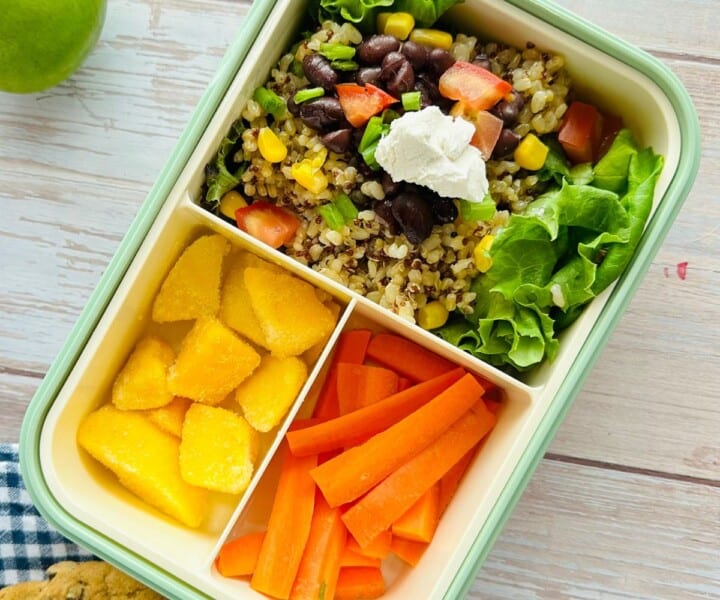 quinoa burrito bowl in a bento box with frozen mango chunks and carrot sticks