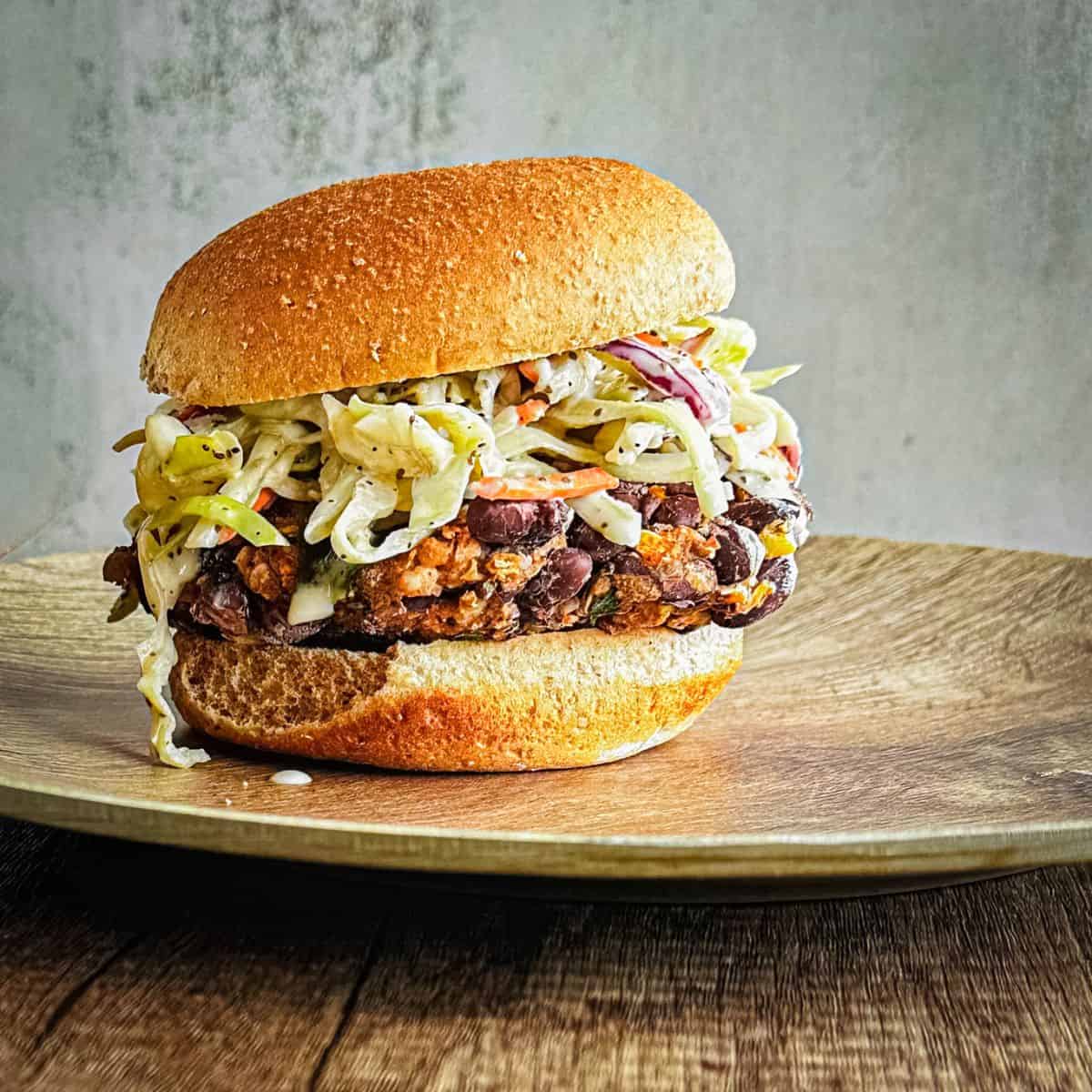 chipotle black bean burger on a plate. Burger is topped with vegan coleslaw