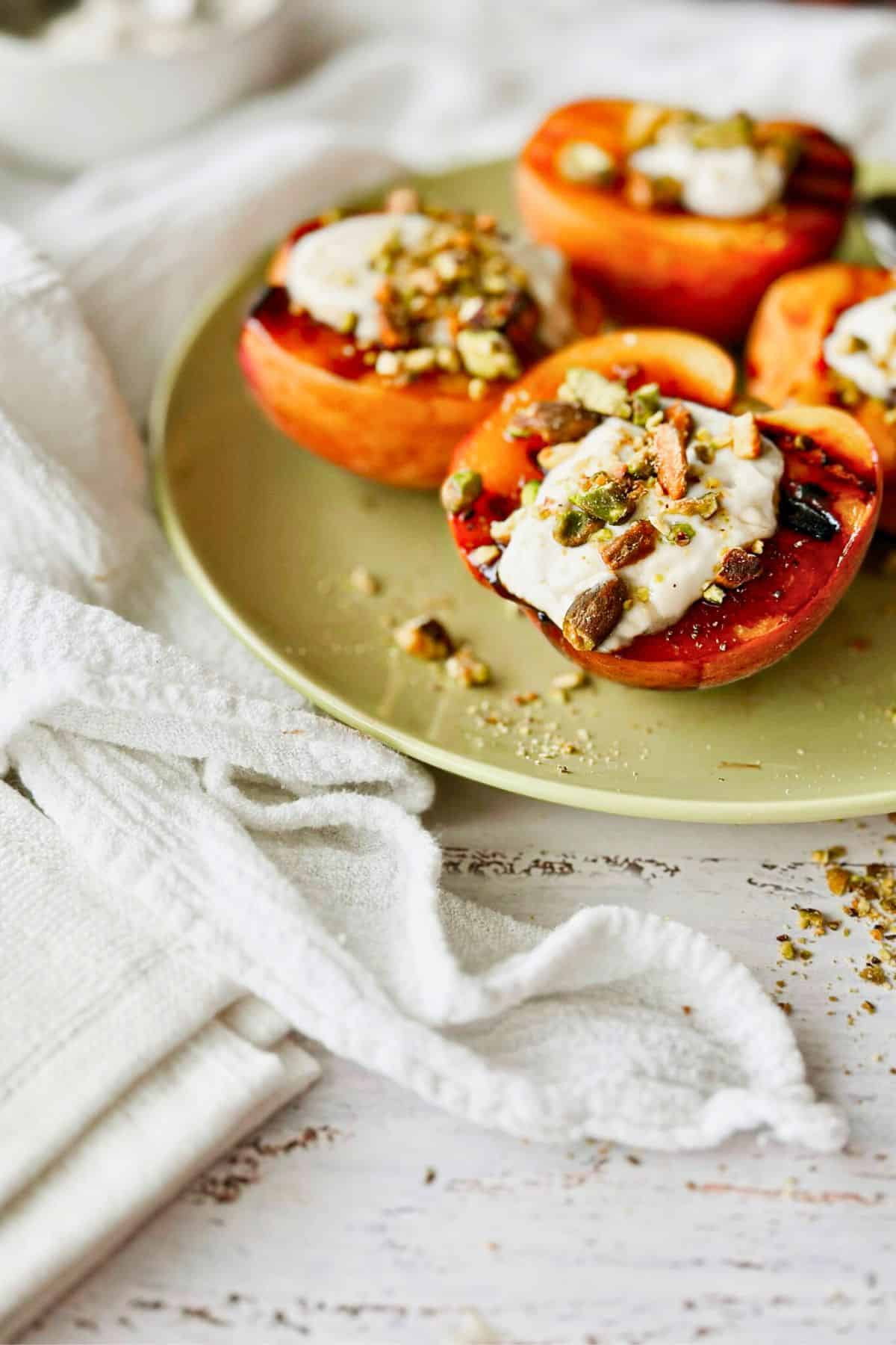 4 halves of Grilled Peaches With Creamy Vegan Mascarpone and Pistachios on a plate