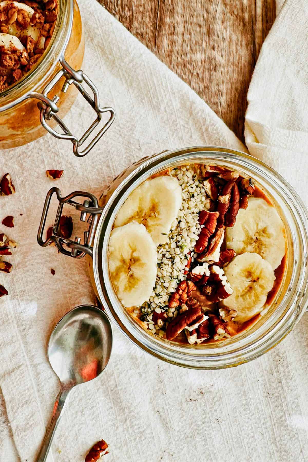 vegan high protein pumpkin overnight oats topped with bananas, hemp seeds, and pecans