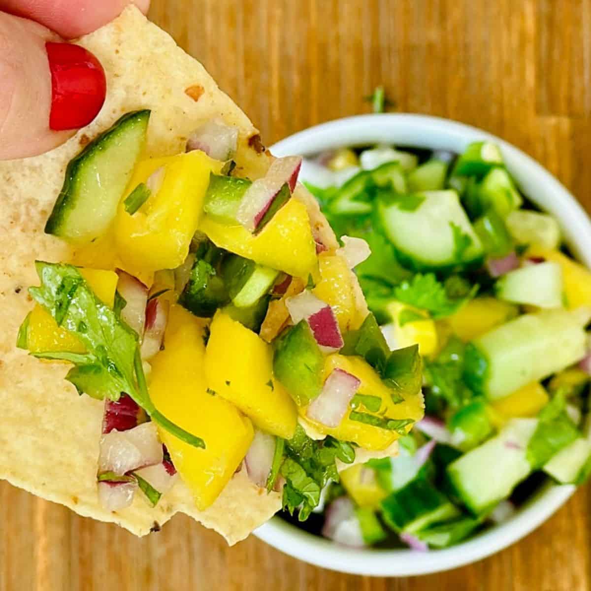 hand holding a chip with mango cucumber salsa