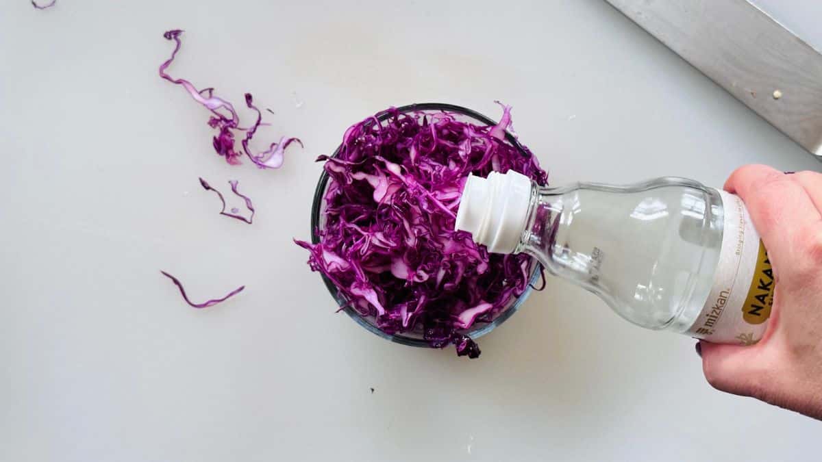 hand holding a bottle of vinegar pouring into a bowl of red cabbage
