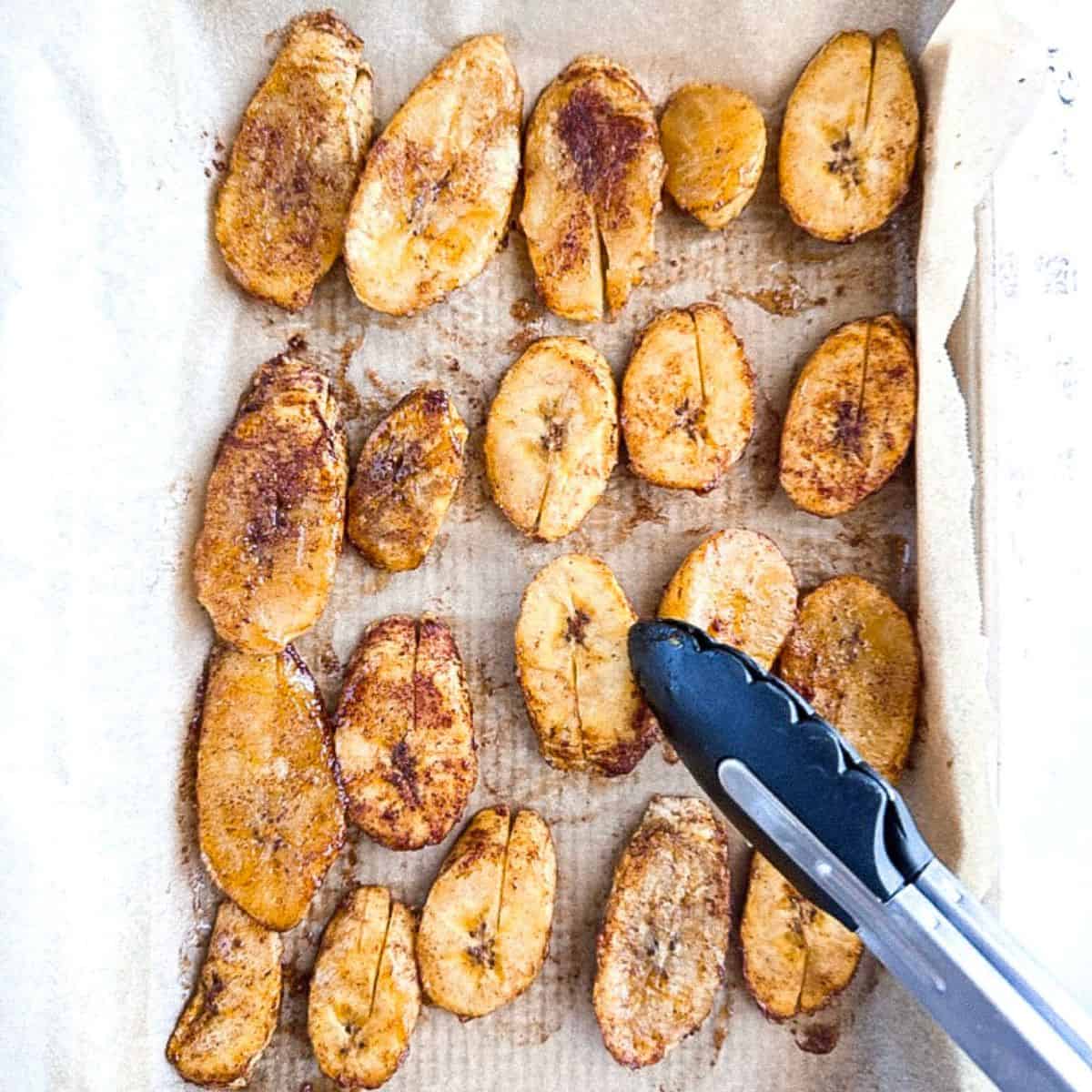 plantains on a baking tray being flipped; top view