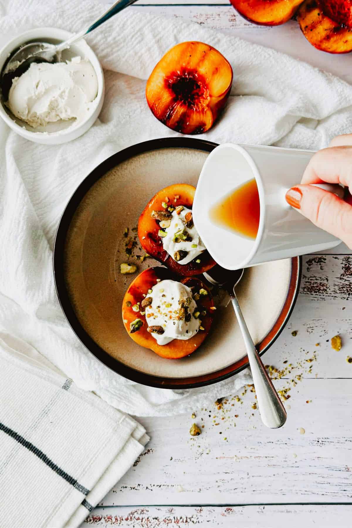 pouring maple syrup on grilled peaches and vegan mascarpone