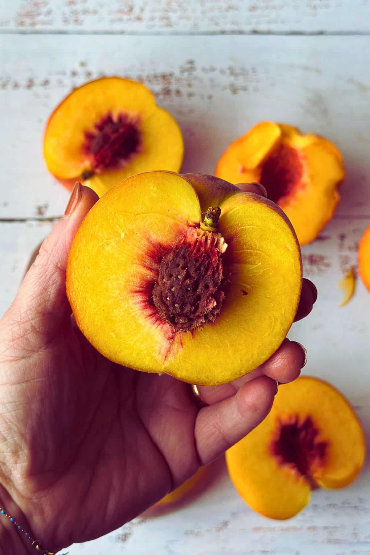 Preparing peaches for grilled peaches with vegan mascarpone. Hand holding a cut ripe peach with pit