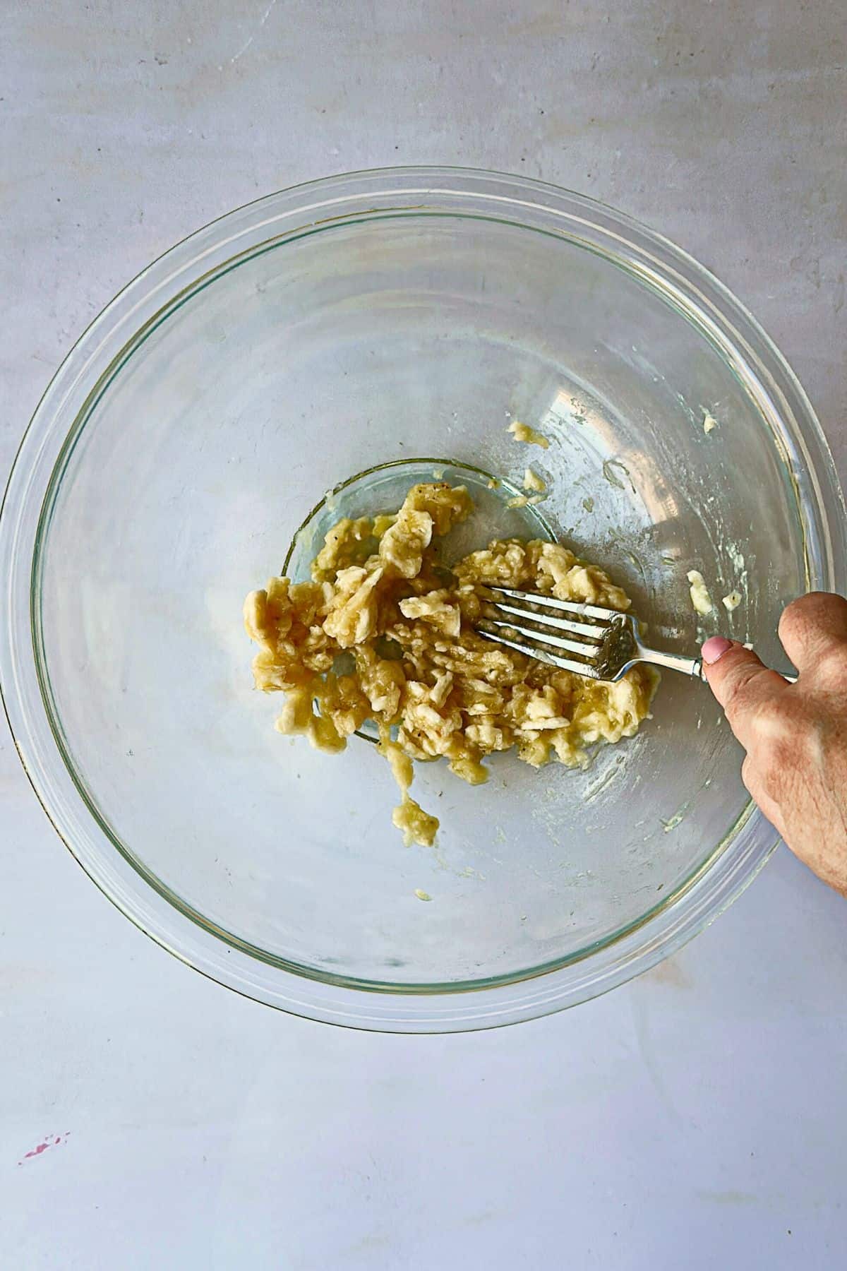 overview of smashing bananas with a fork for overnight oats in a clear bowl.