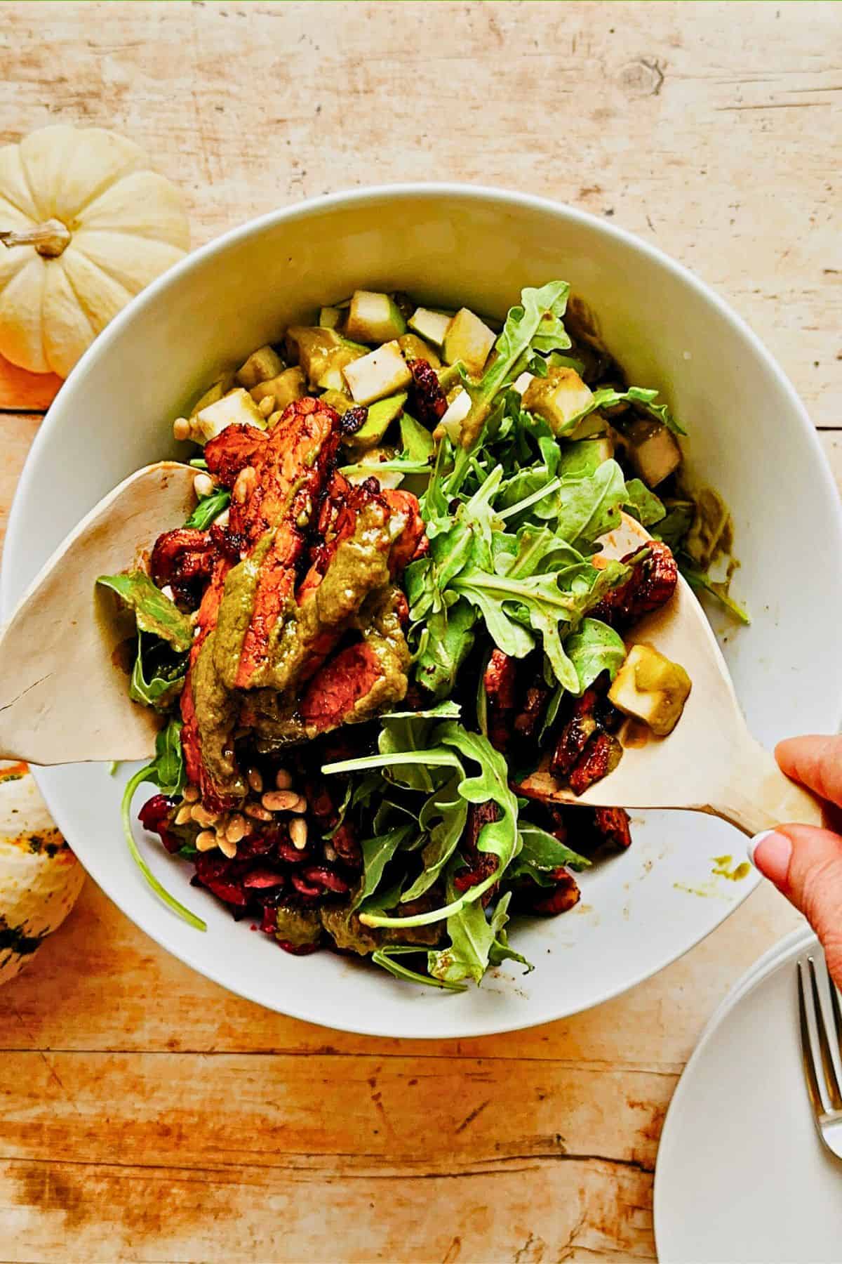 tossing arugula salad with pumpkin vinaigrette in a bowl