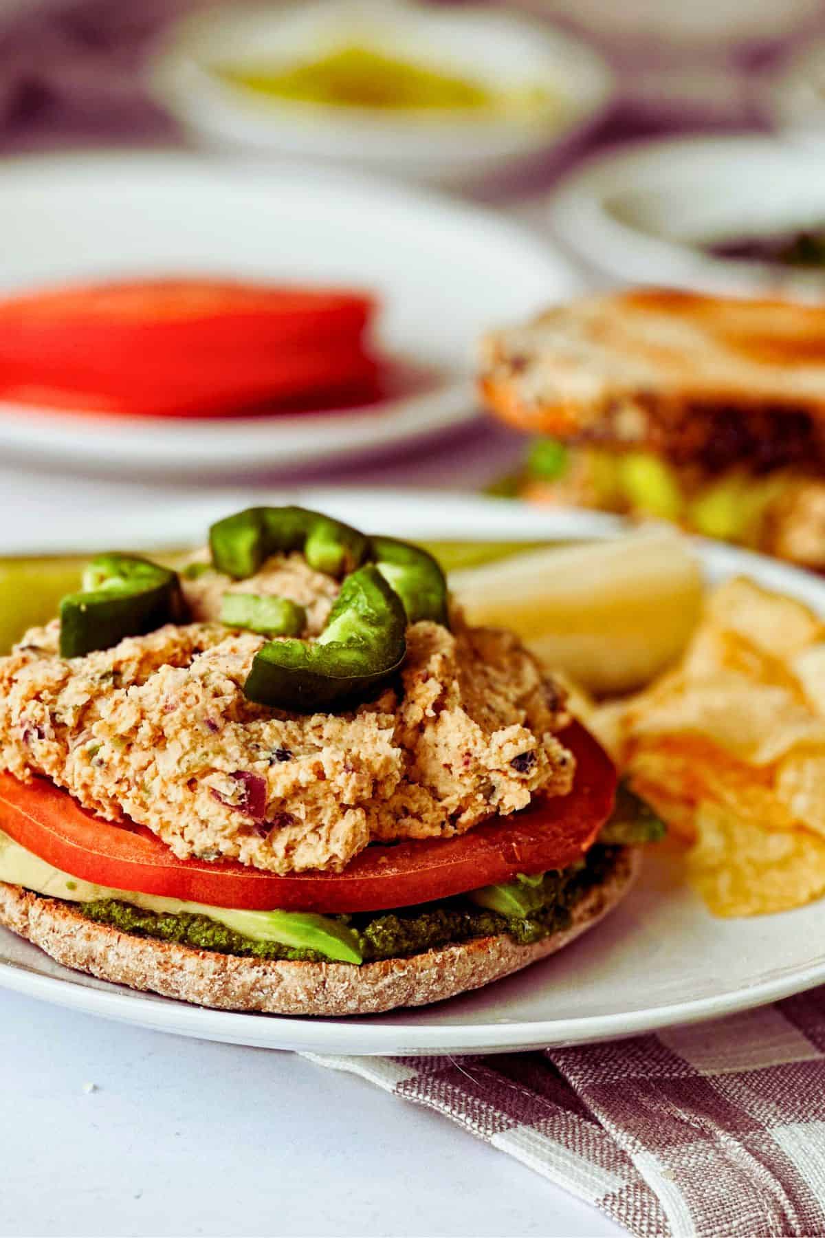 side view of tunacado sandwich - see the layers of pesto, tomato, vegan tuna, and jalapeno on top