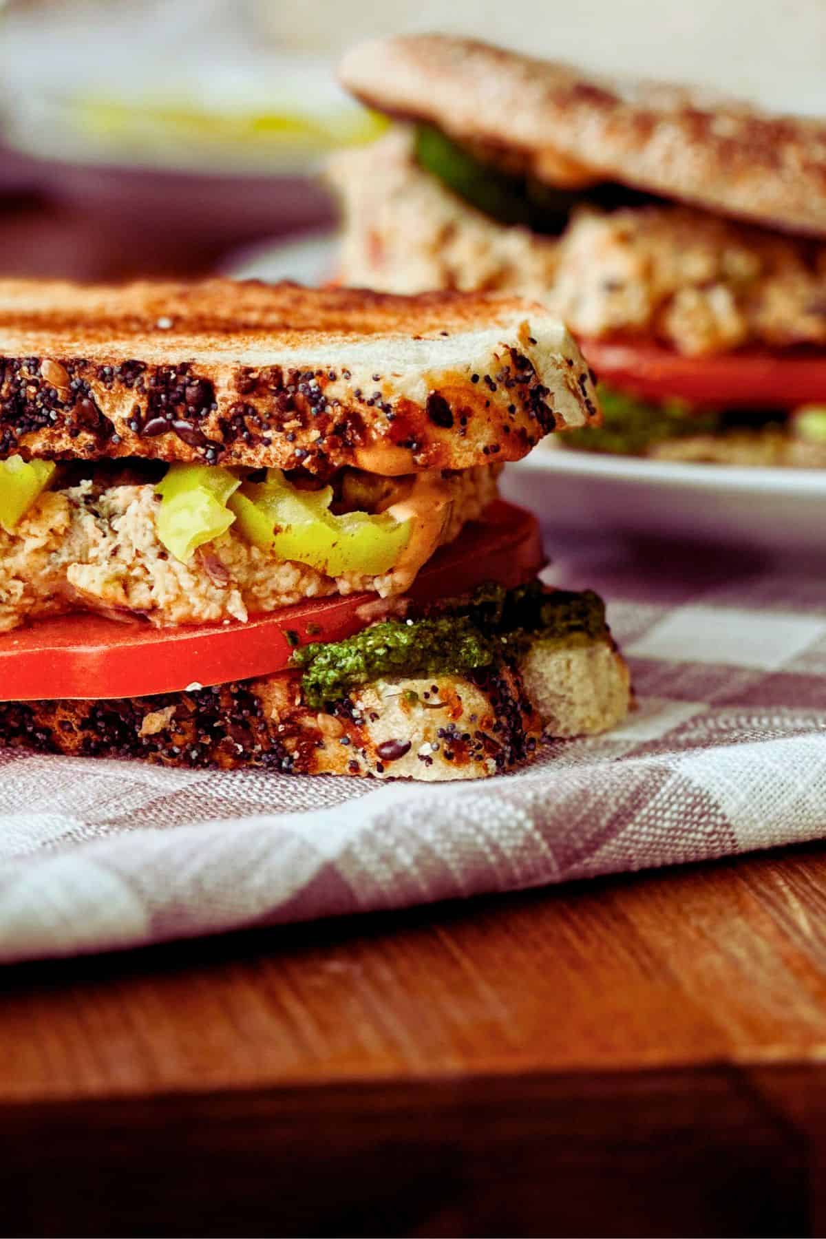 tunacado sandwich on sourdough bread; side view of the layers with pesto, avocado, vegan chipotle aioli, vegan tuna, and banana peppers