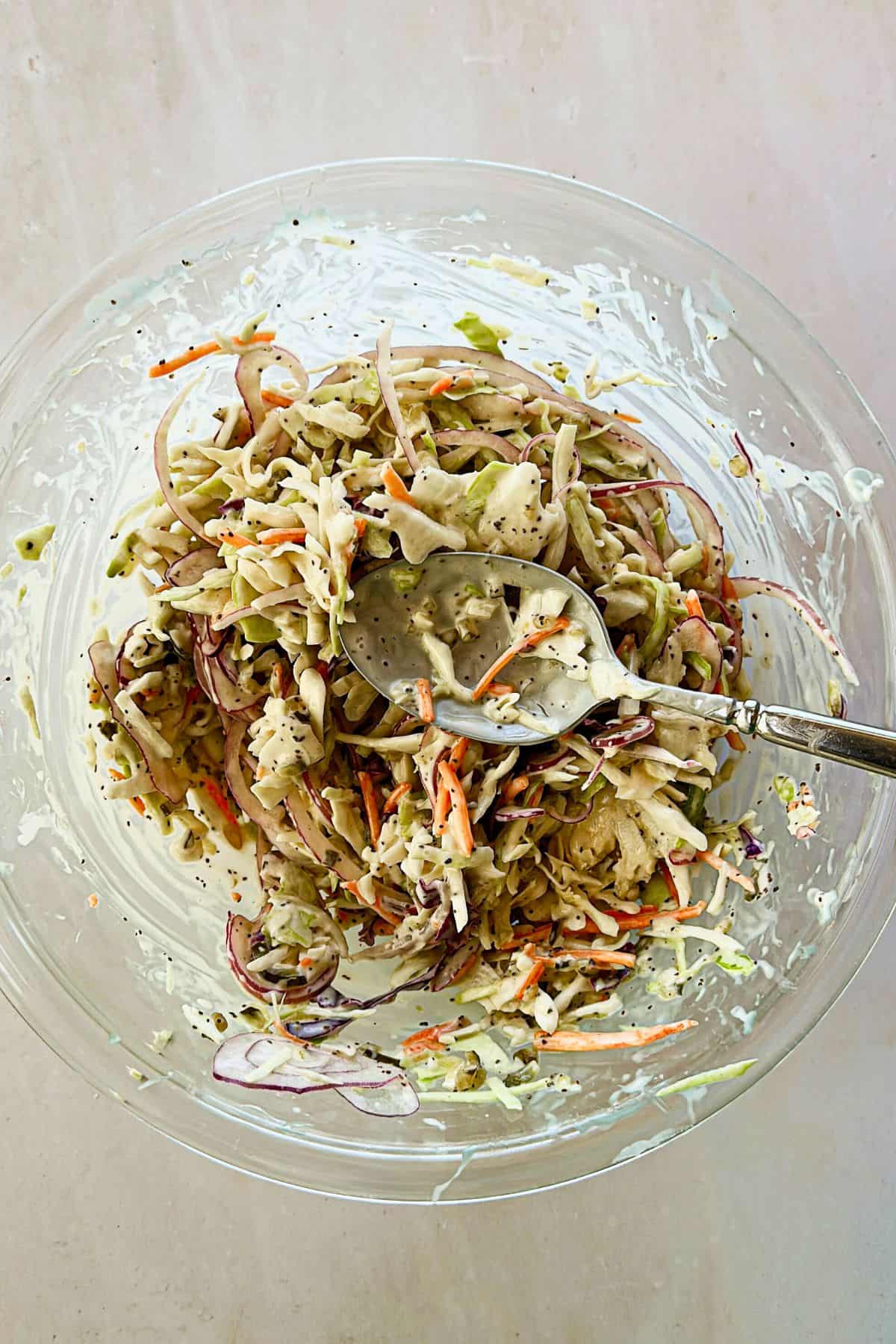 vegan coleslaw in a clear bowl being tossed with a spoon
