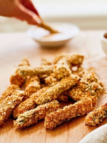 side view of vegan panko baked zucchini fries on a cutting board.