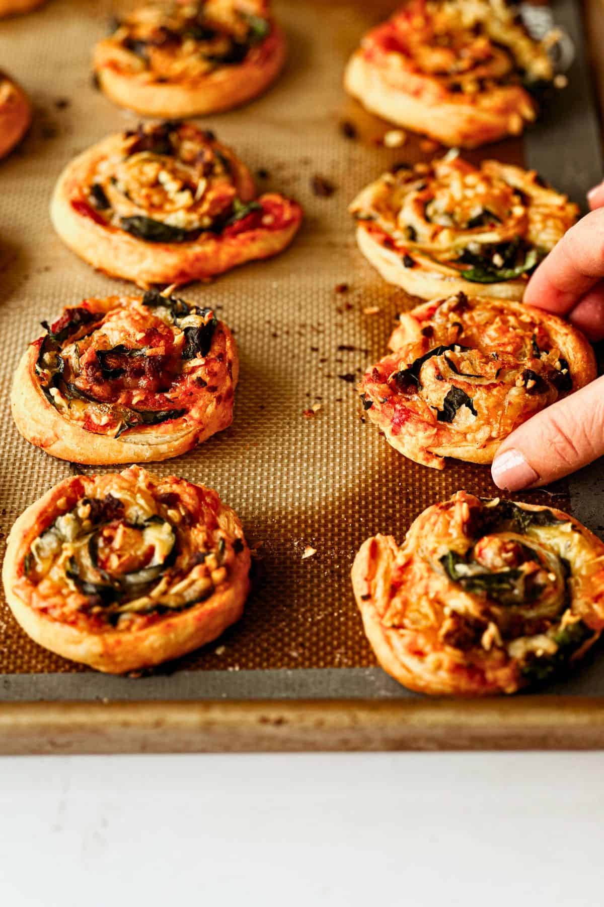 hand reaching in to grab a pizza roll from baking tray