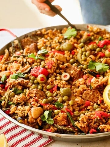 side view of vegan spanish paella in a pan with a hand holding a fork digging into the pan.