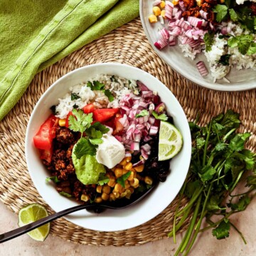 top view of vegan taco bowl with a spoon in the bowl. caddy cornered is another plate with vegan taco bowl ingredients.
