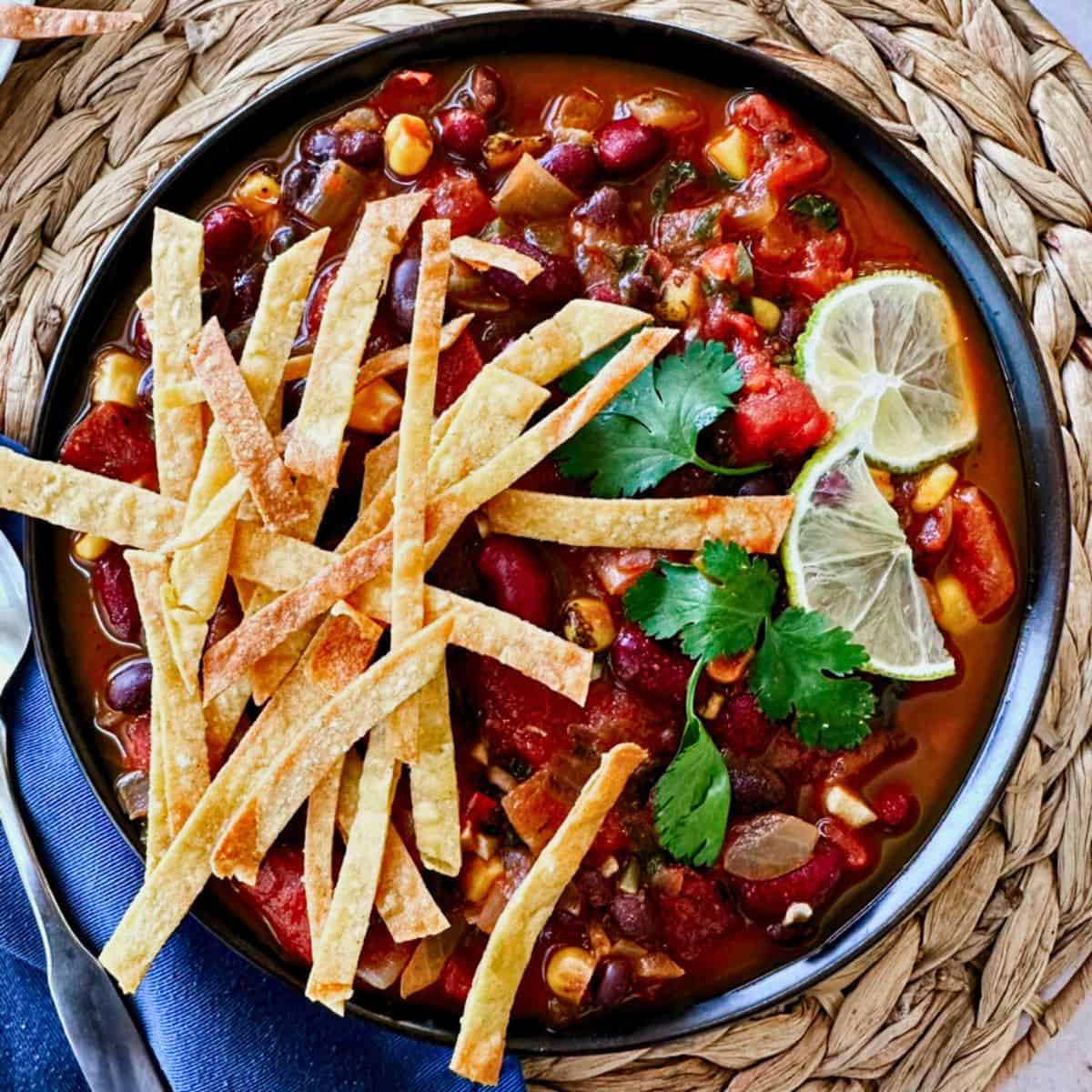 vegan tortilla soup with baked tortilla chips in a dark bowl; top view
