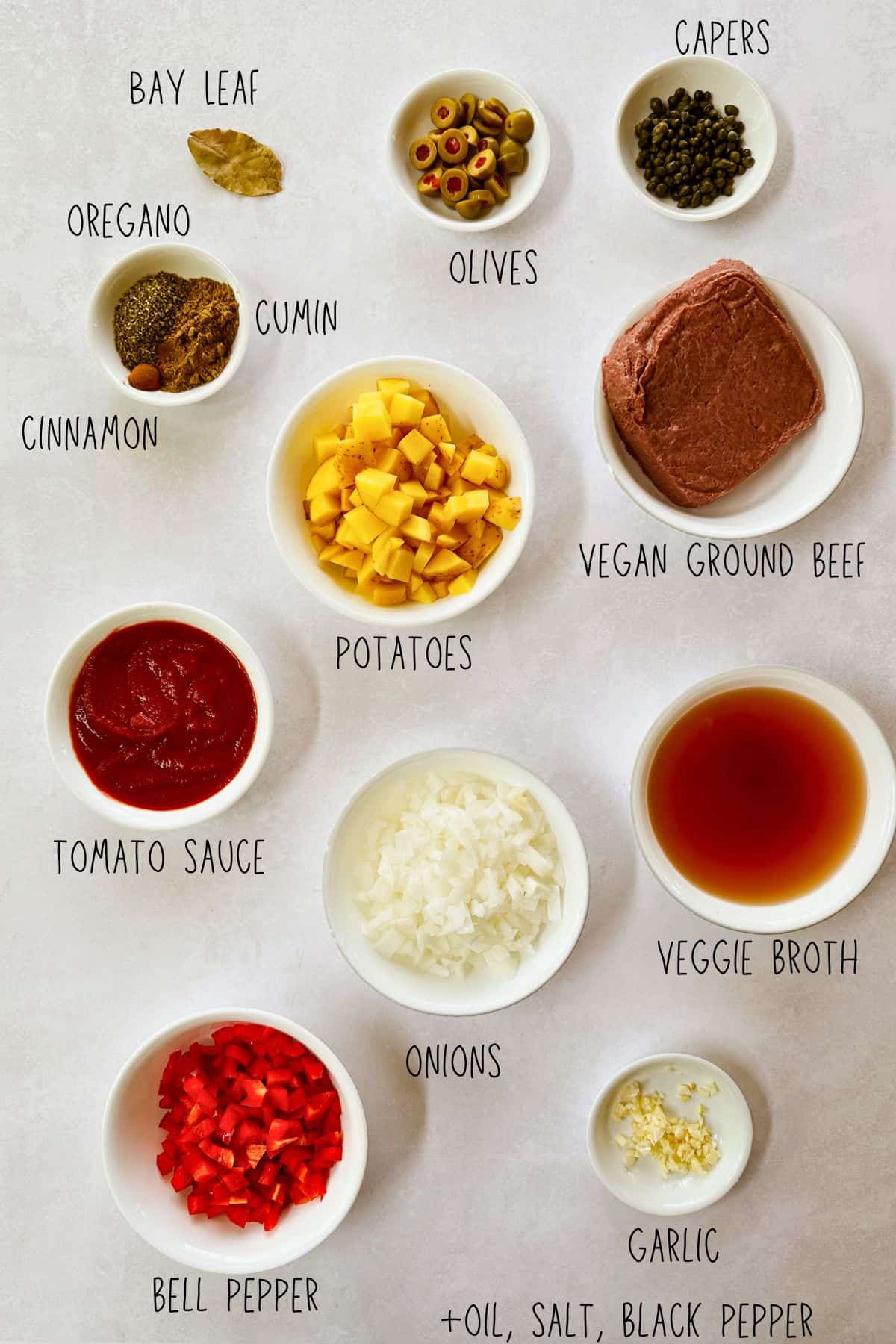 Flat lay of ingredients for vegan Cuban picadillo, including Impossible plant-based ground beef, diced potatoes, bell pepper, onion, garlic, tomato sauce, veggie broth, olives, capers, bay leaf, oregano, cumin, and cinnamon.