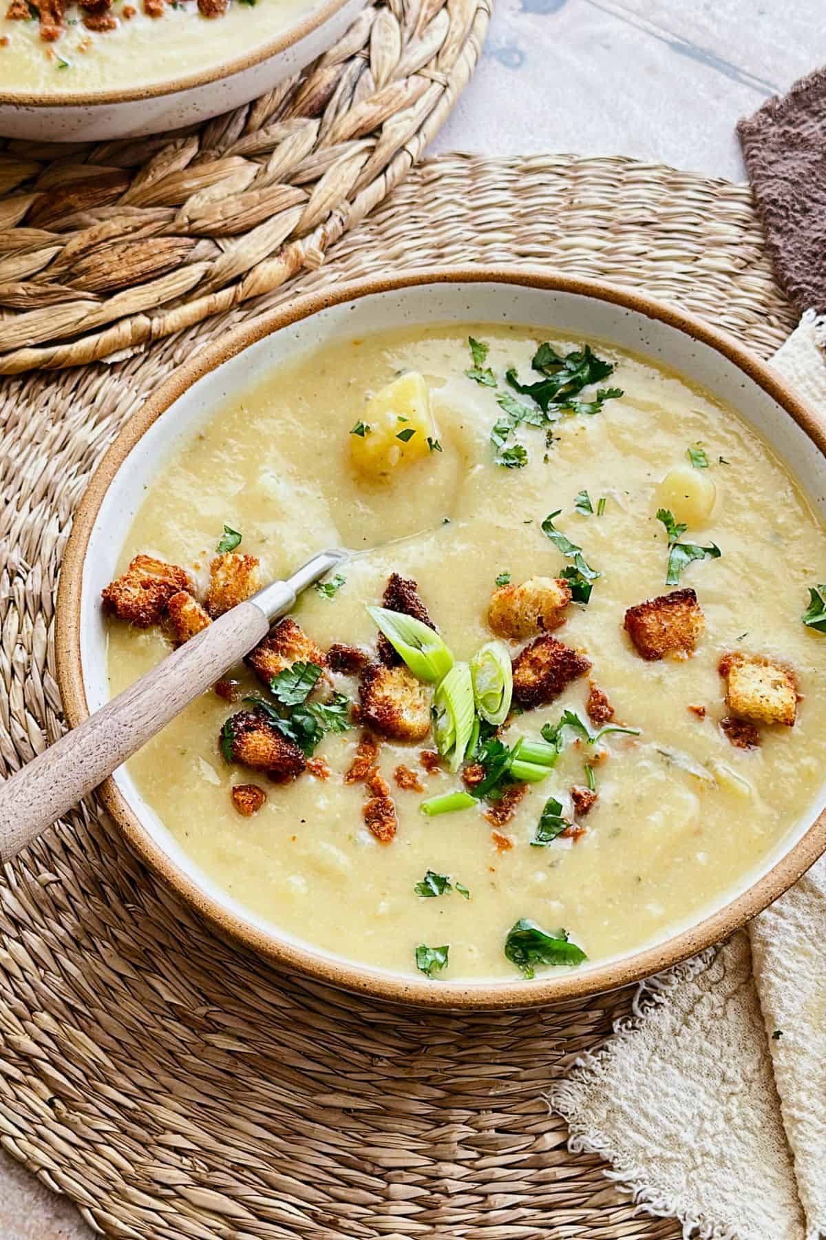Bowl of creamy cauliflower potato soup topped with golden croutons, fresh parsley, and green onions, with a spoon ready for serving.
