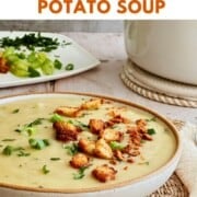 Easy-to-make creamy cauliflower potato soup in a rustic bowl topped with golden croutons and green onions, served with fresh herbs on the side. Title says "How to Make Cauliflower Potato Soup, Creamy Delicious."