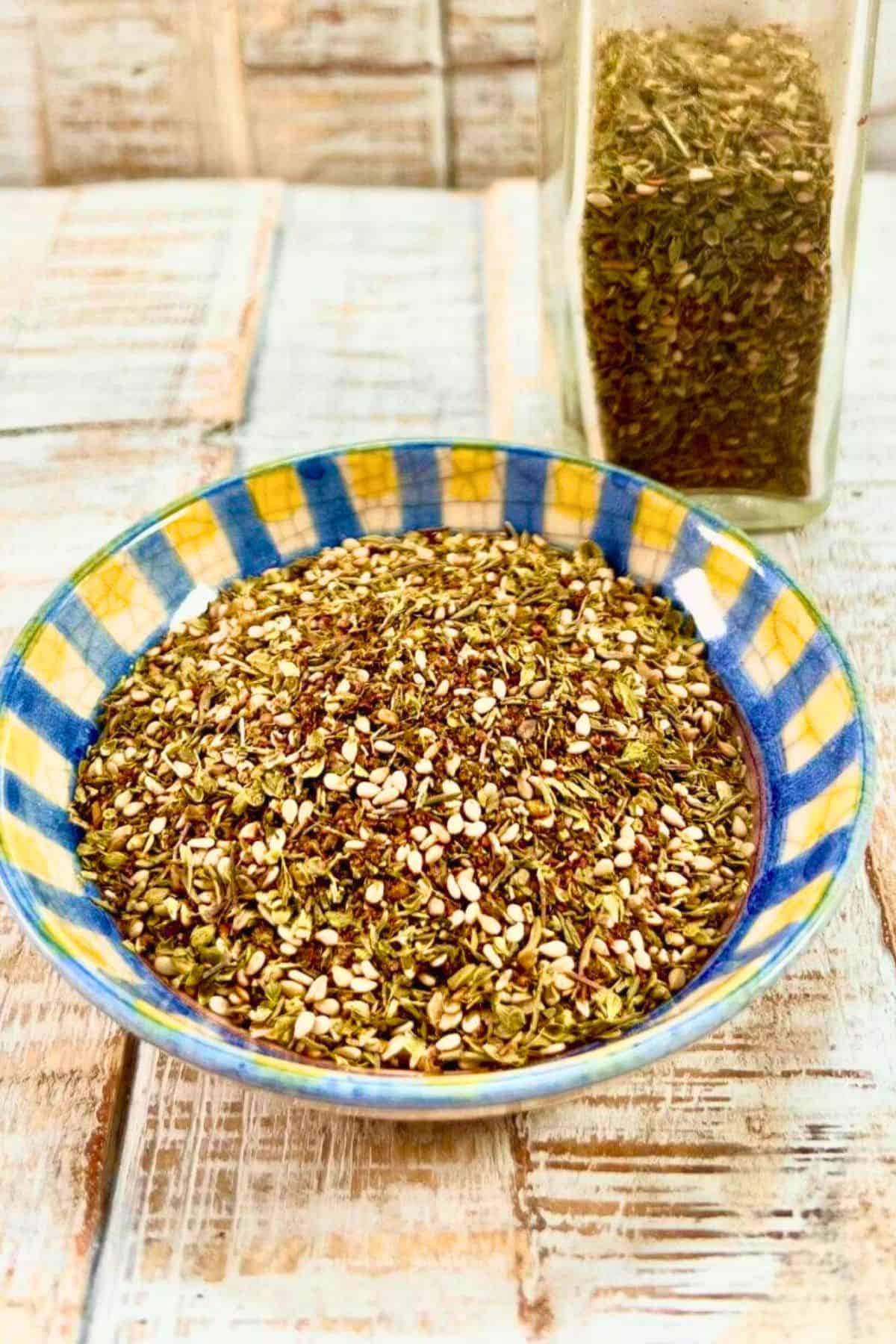 zaatar in a colorful bowl with a glass bottle behind it containing more of the spice blend.