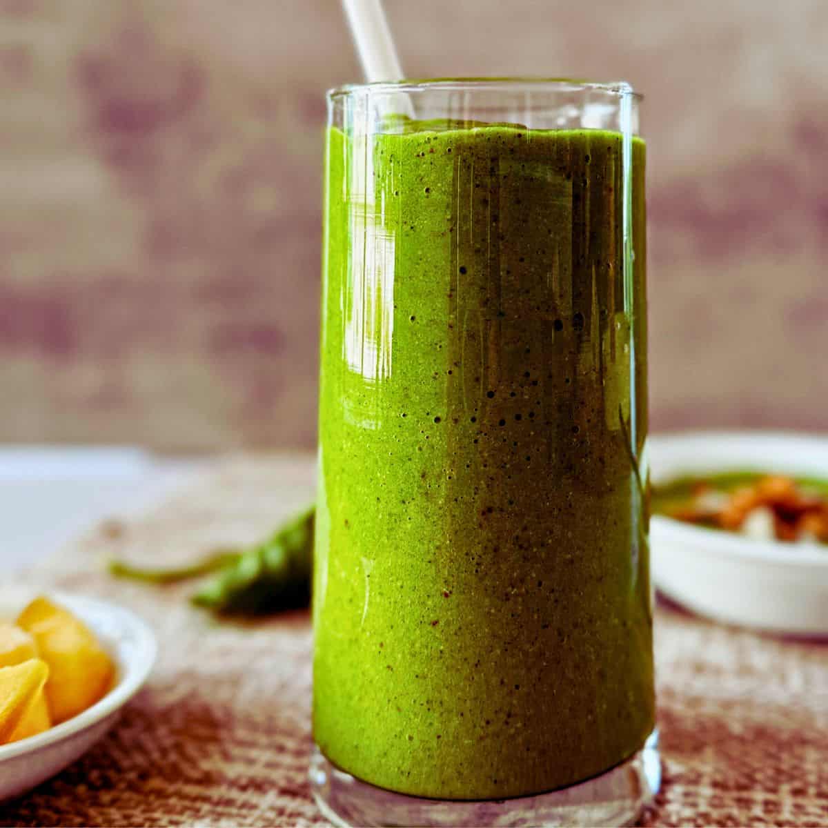 side view of a glass of Mango Kale Smoothie -Smoothie King Copycat with a straw.