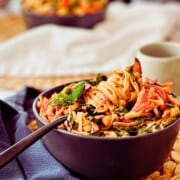 top view of Thai Peanut Noodle Salad with a fork wrapped in noodles. Person is sitting in the back eating a bowl of peanut noodles.